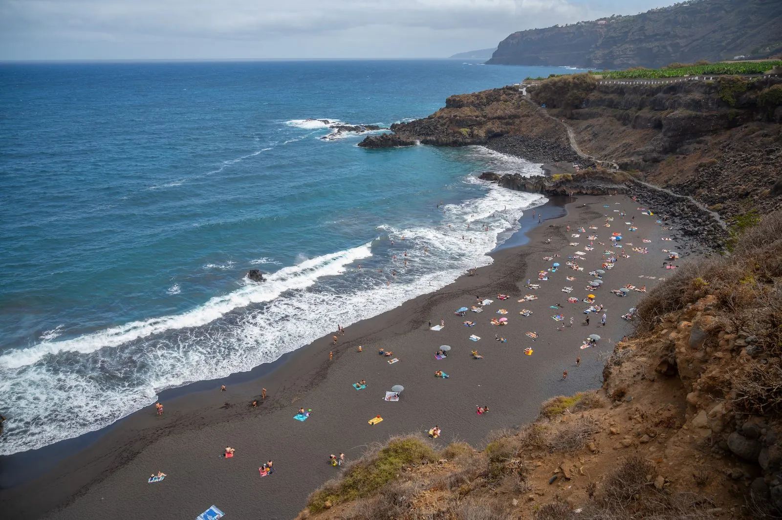 The black volcanic sand of Playa El Bollullo below green cliffs near La Orotava, Tenerife