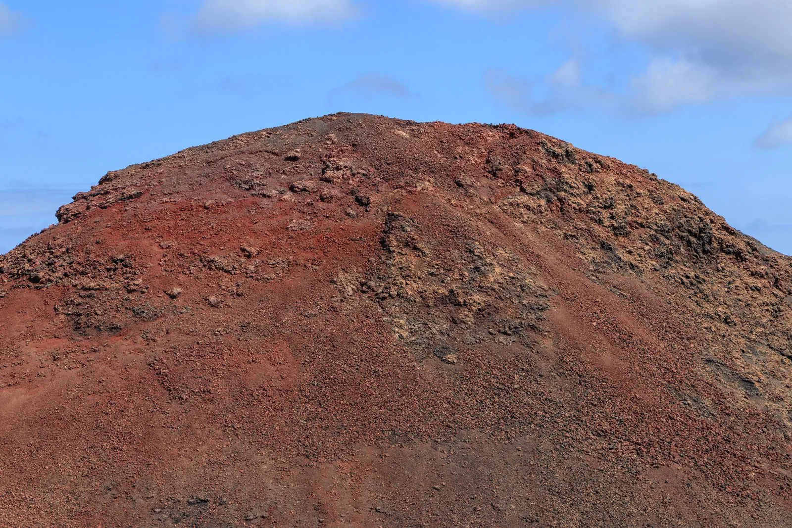 A reddish volcanic cone in the barren lava fields of Timanfaya National Park, Lanzarote